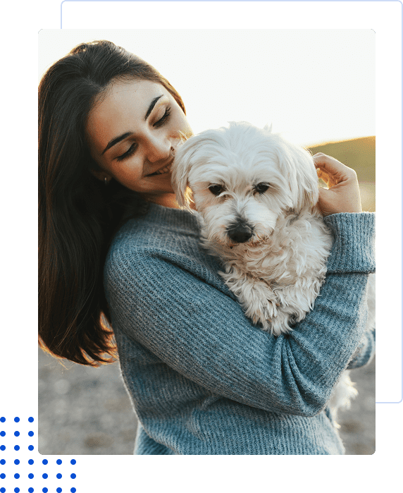 A woman happily hugging her small white dog outdoors.